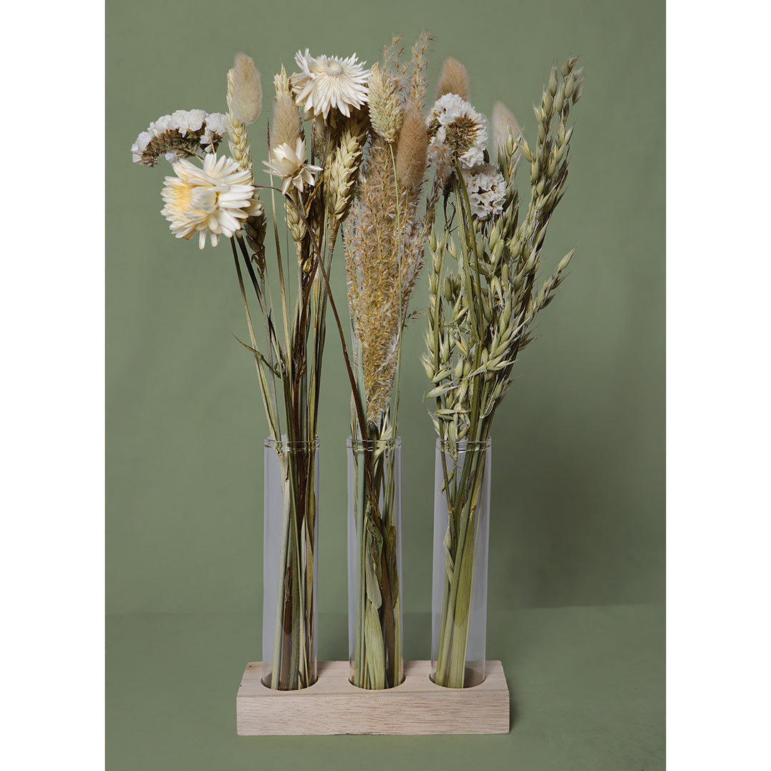 Three clear glass vases with dried flowers on a wooden base against a green background