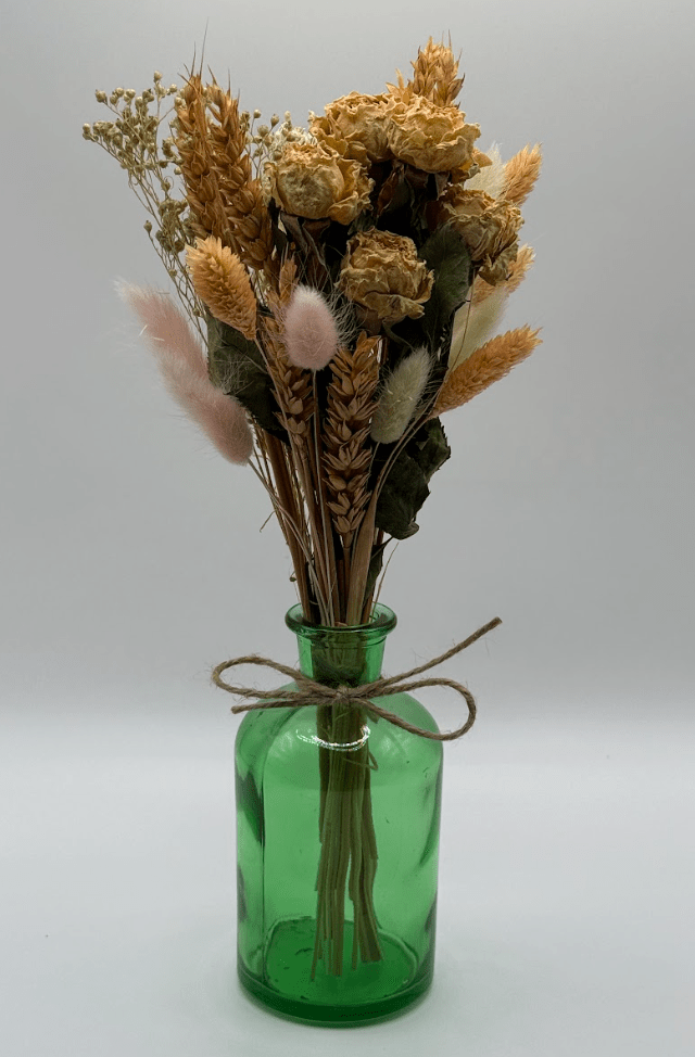 Green glass bottle with dried flowers on a white background