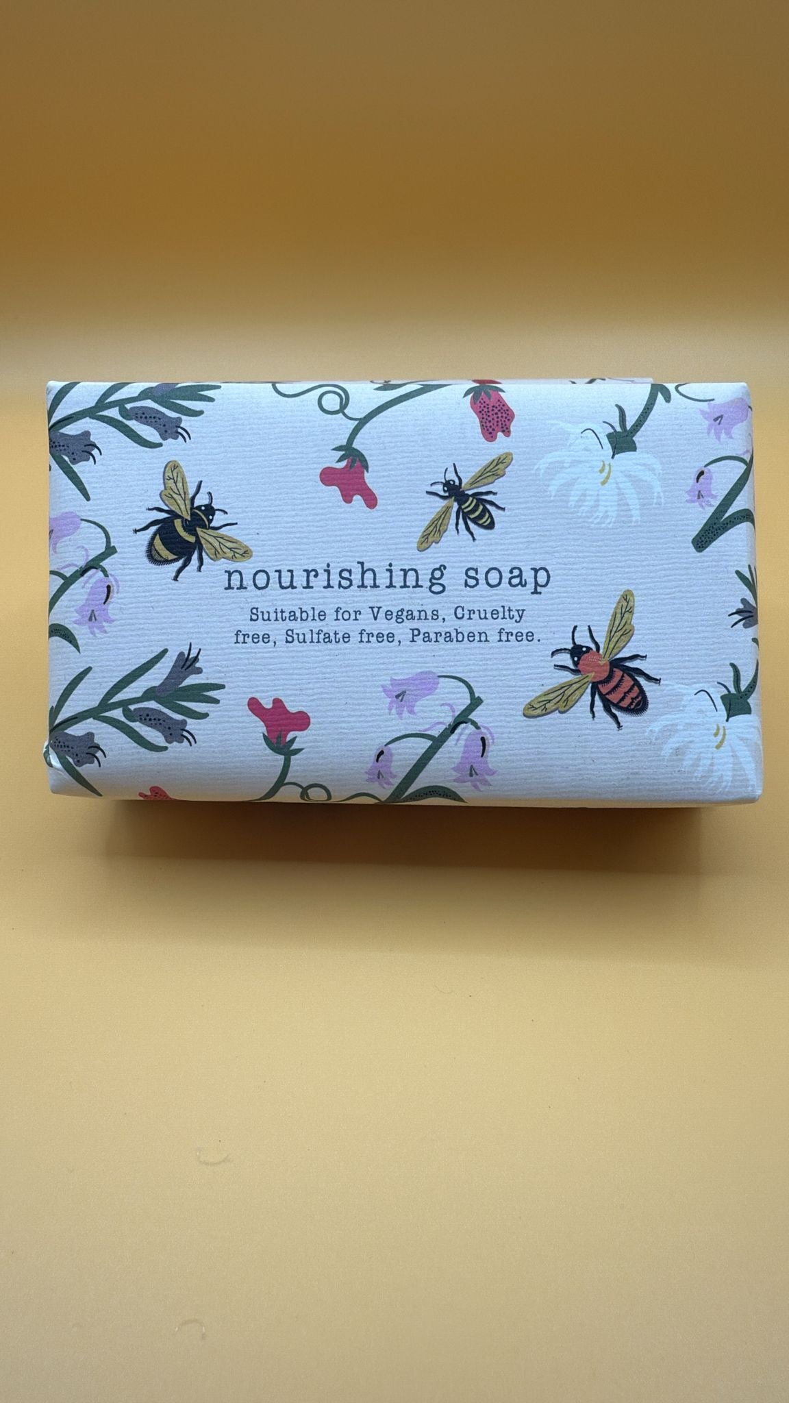 Bar of soap with decorative packaging featuring bees and plants on a yellow background