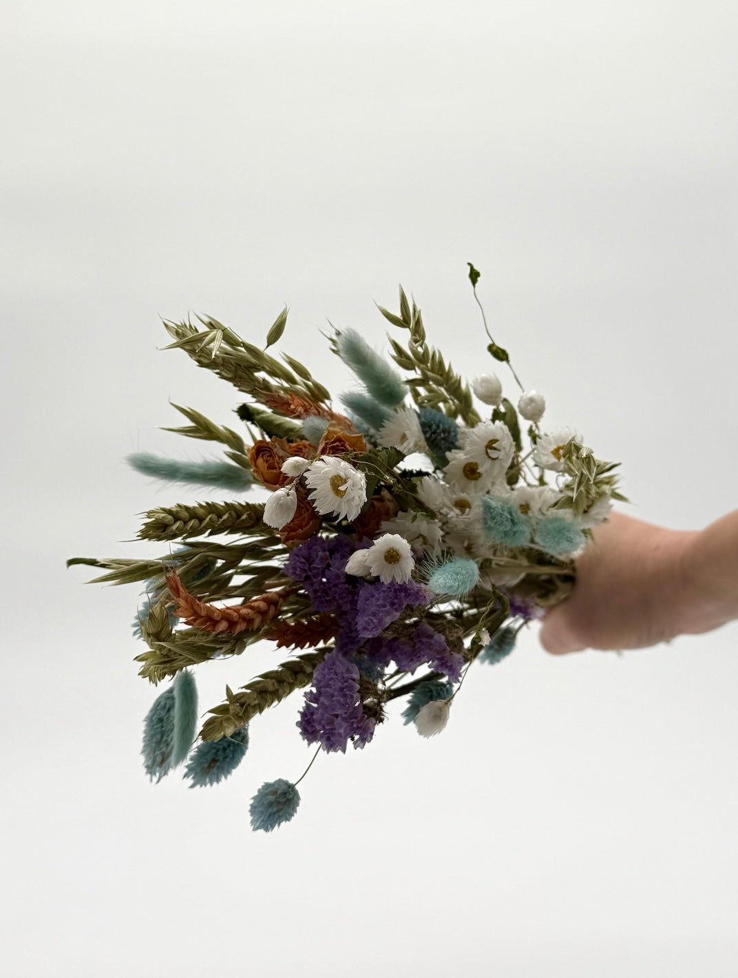 Bouquet of dried flowers held by a hand against a plain background