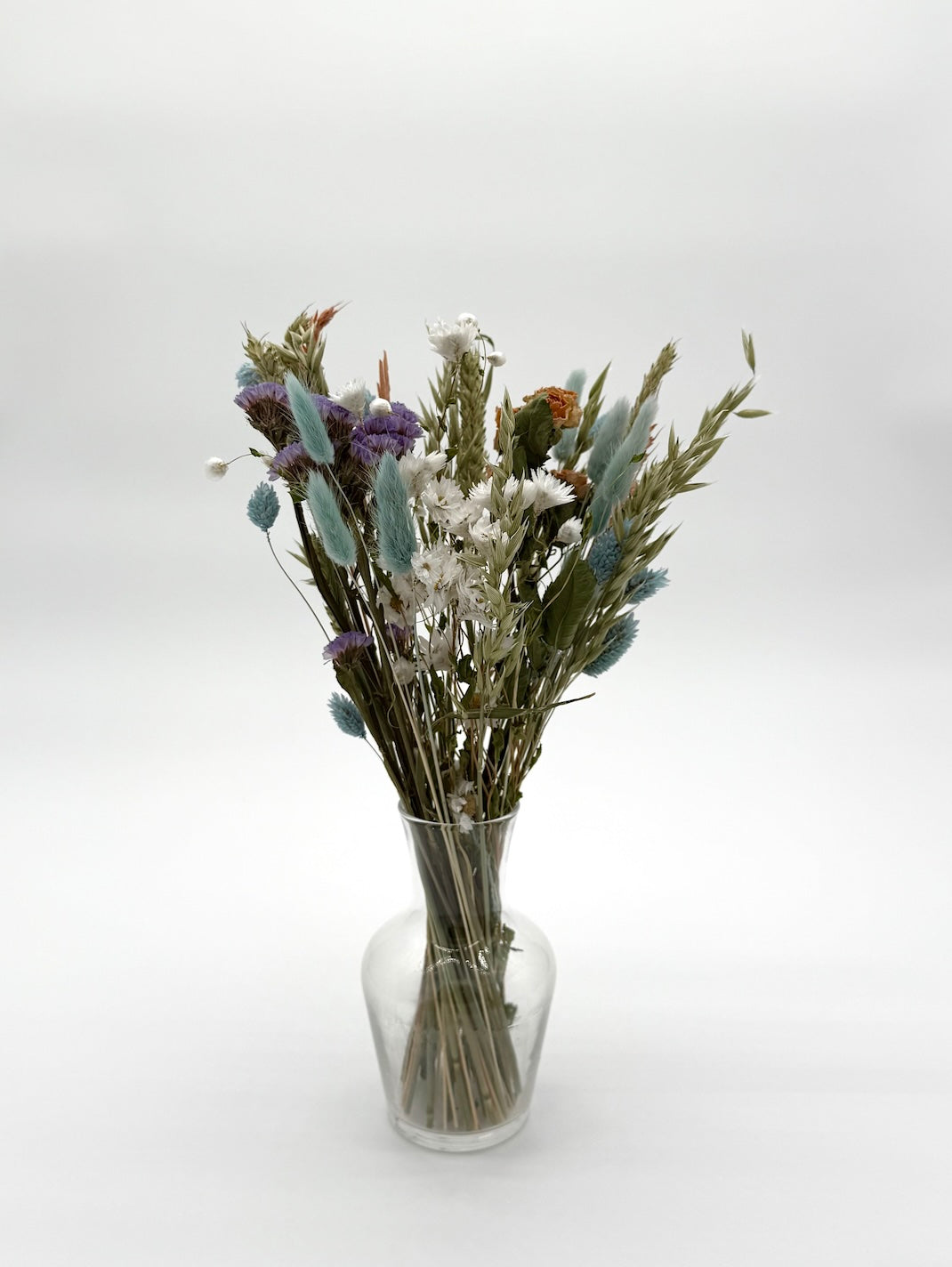Bouquet of dried flowers in a clear glass vase on a white background