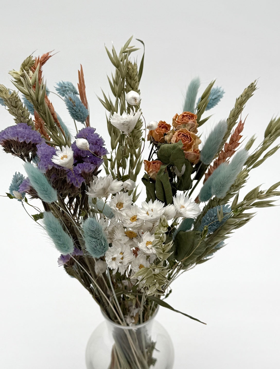 Bouquet of dried flowers in a clear vase on a white background