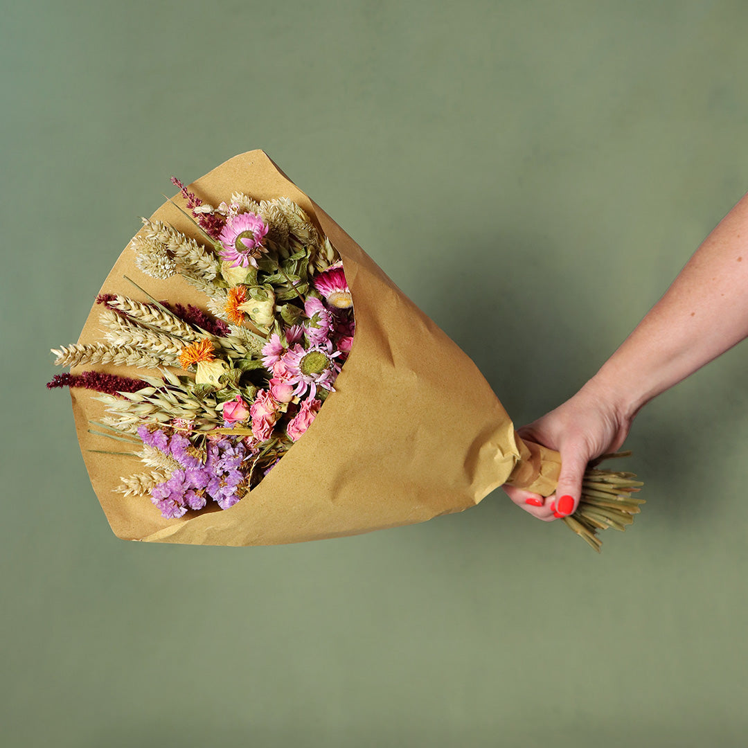 Bouquet of dried flowers wrapped in brown paper held by a hand against a green background