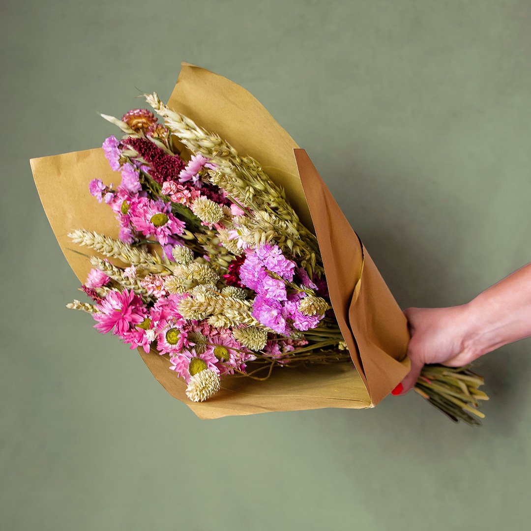 Bouquet of flowers wrapped in brown paper held by a hand against a green background