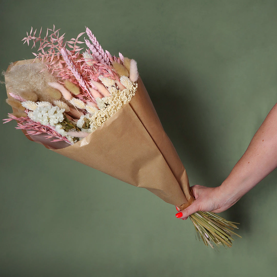 Bouquet of flowers wrapped in brown paper held by a hand against a green background