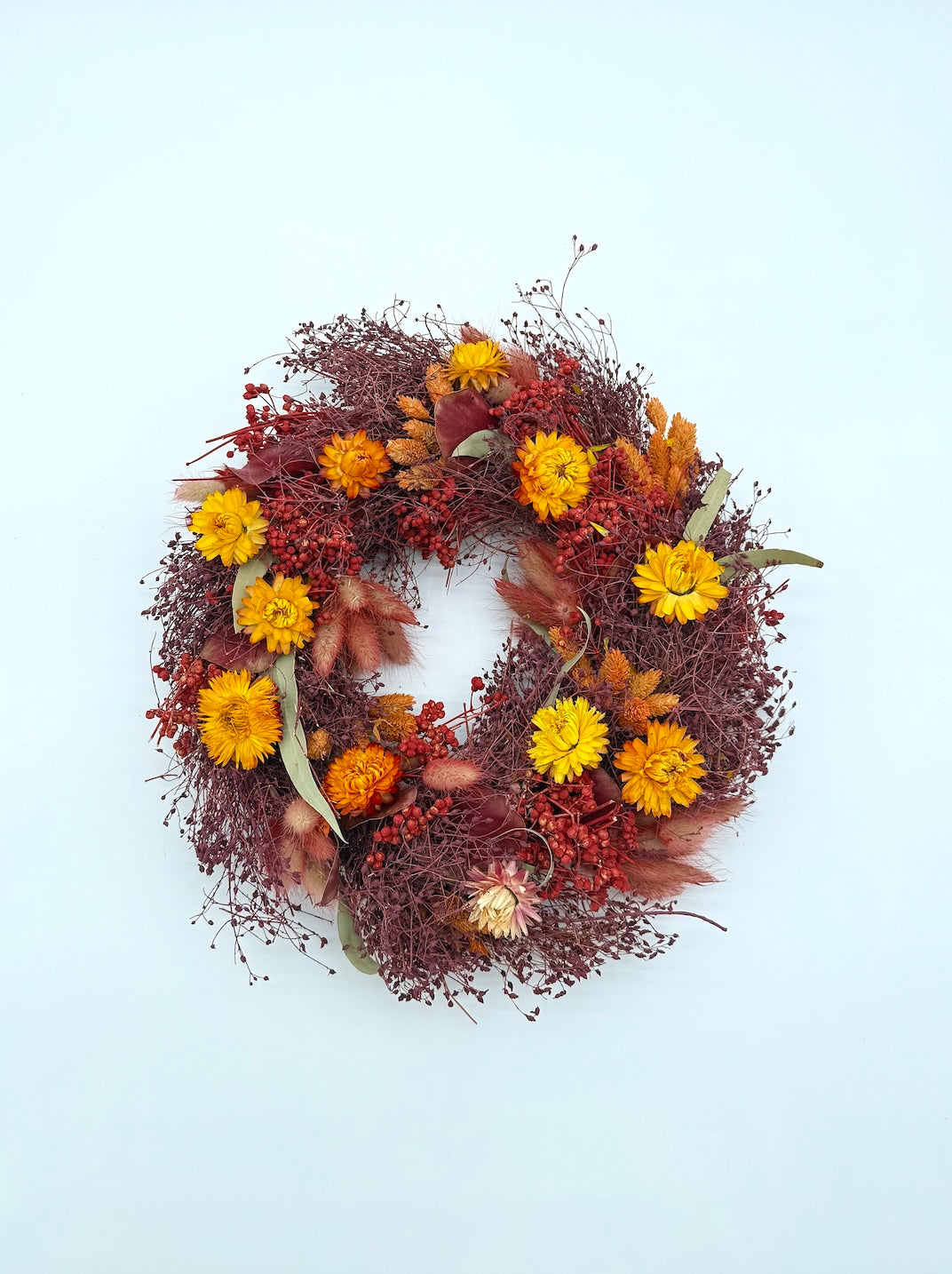 Autumn-themed wreath with yellow flowers and red berries on a light blue background