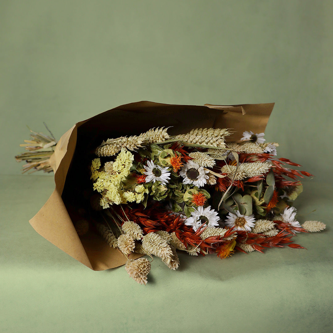 Bouquet of dried flowers wrapped in brown paper on a green background