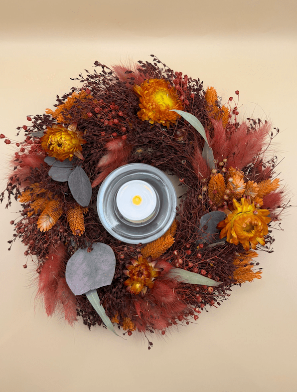 Decorative wreath with autumnal flowers and a candle on a beige background