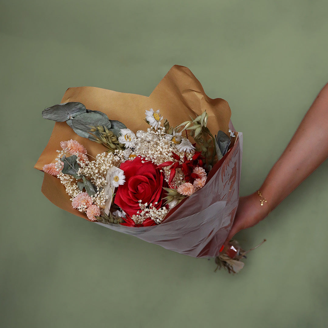 Bouquet of flowers wrapped in brown paper held by a person against a green background