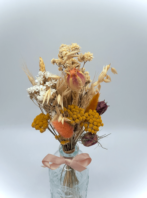 Bouquet of dried flowers in a glass vase with a pink ribbon on a light gray background