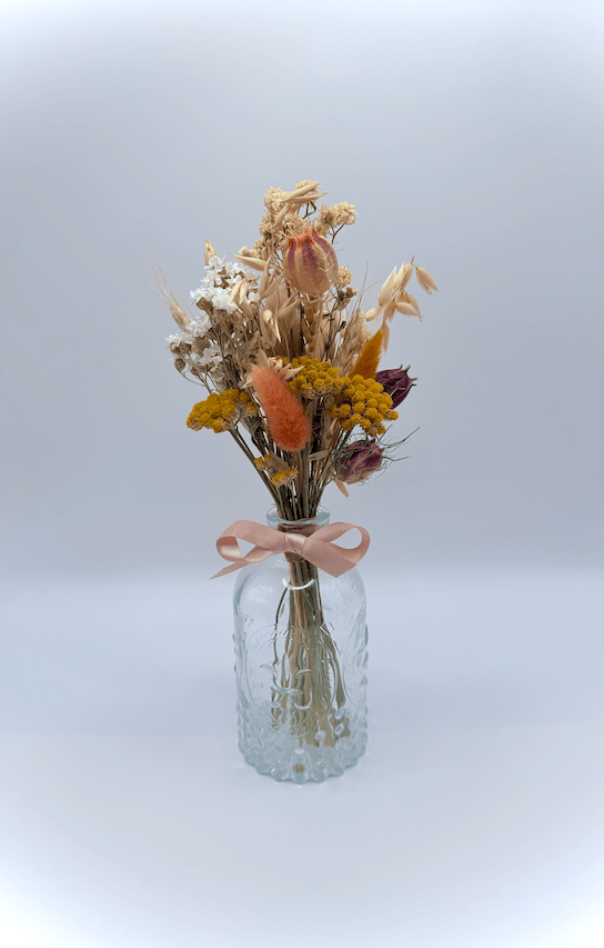 Glass vase with dried flowers and a pink ribbon on a light gray background