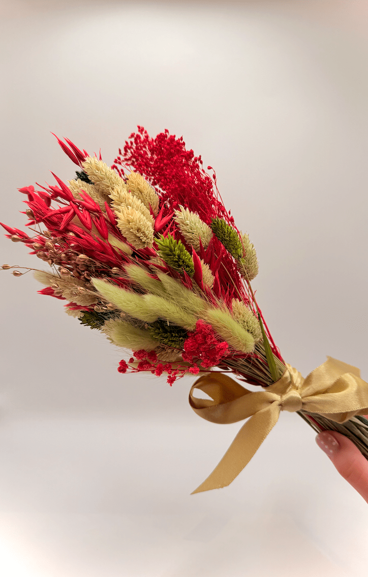 Bouquet of red and green dried flowers with a gold ribbon on a white background