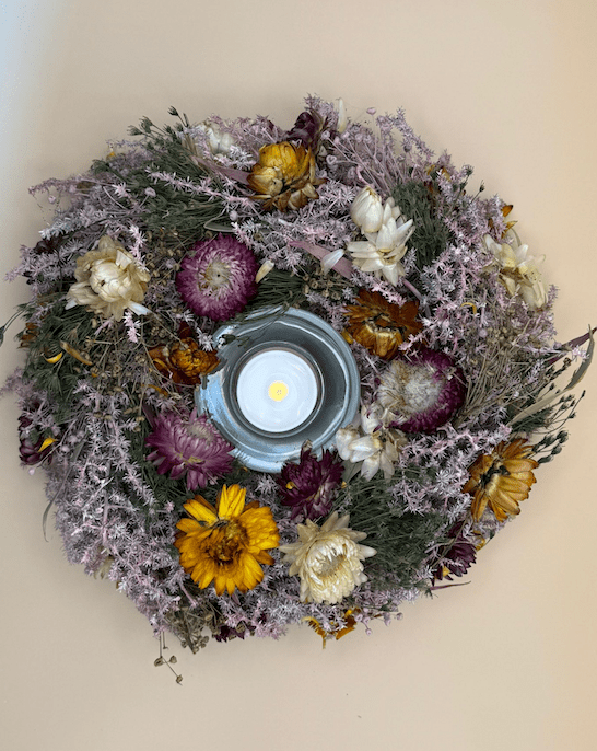 Decorative wreath with dried flowers and a lit candle in the center on a beige background