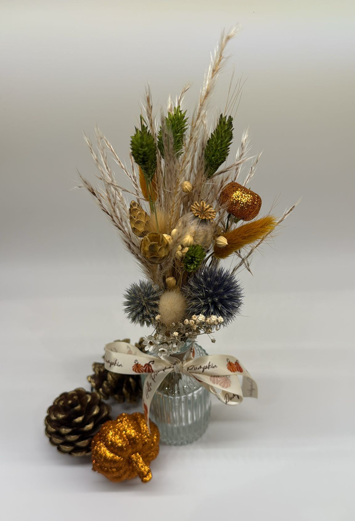 Decorative arrangement with dried plants, pinecones, and decorative ribbons on a white background
