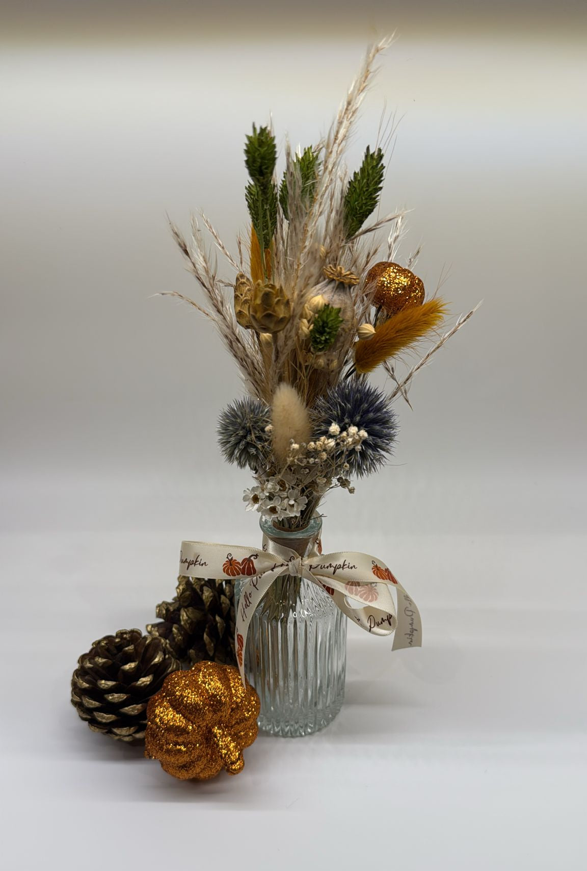 Decorative arrangement with a glass vase, pinecones, and flowers on a white background