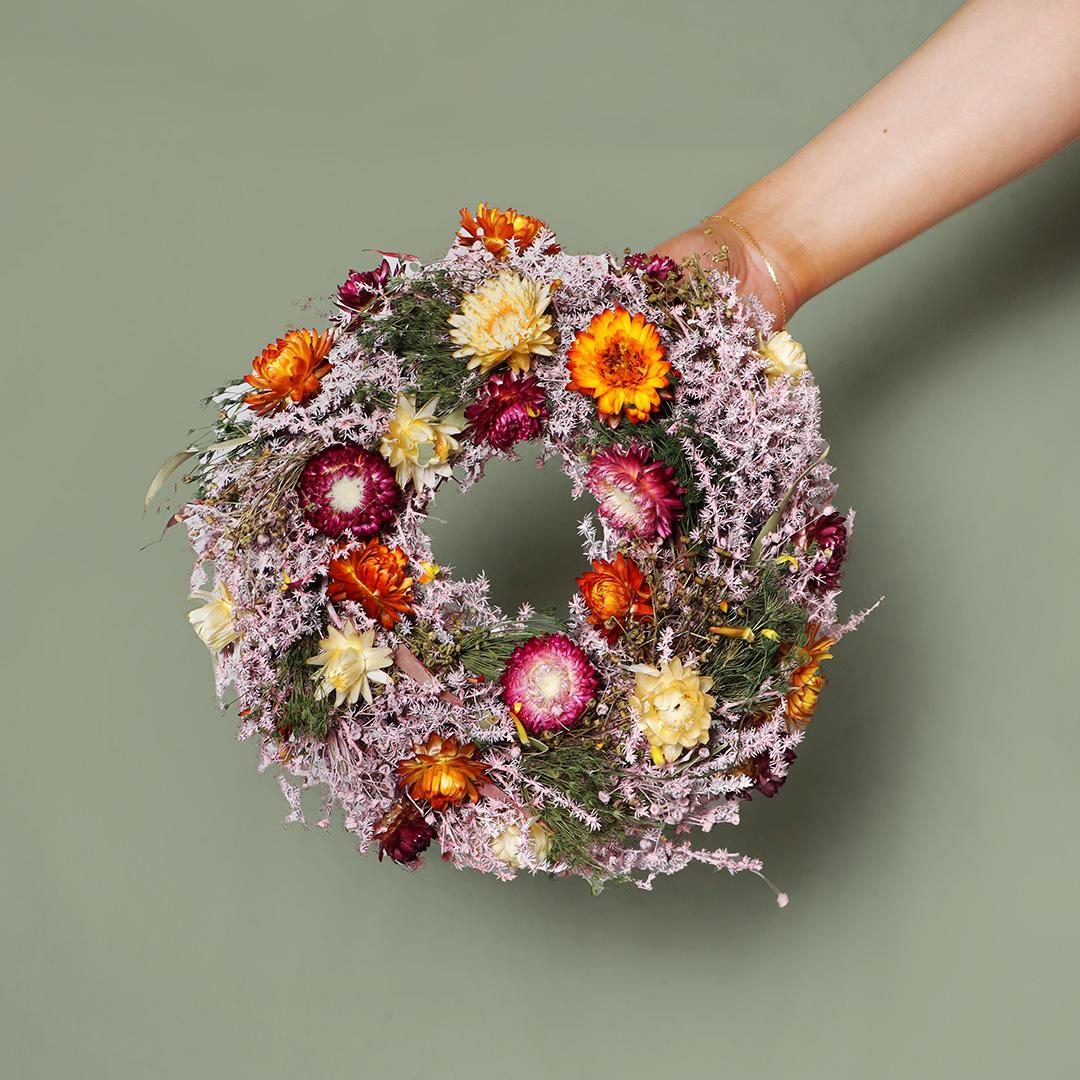 Hand holding a colorful floral wreath against a green background