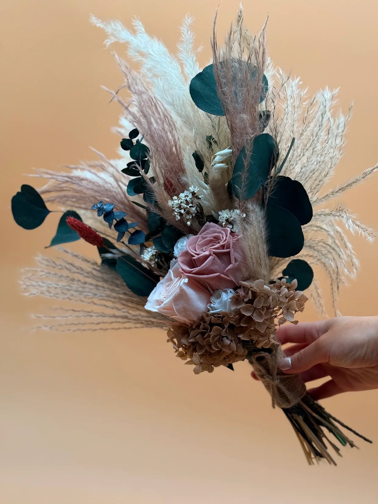 Bouquet of dried flowers and greenery held by a hand against a beige background