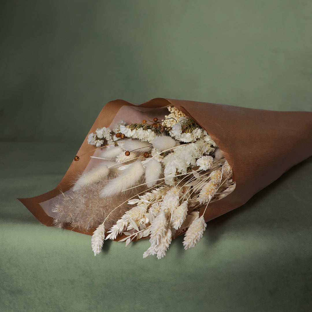 Bouquet of dried flowers wrapped in brown paper on a green background