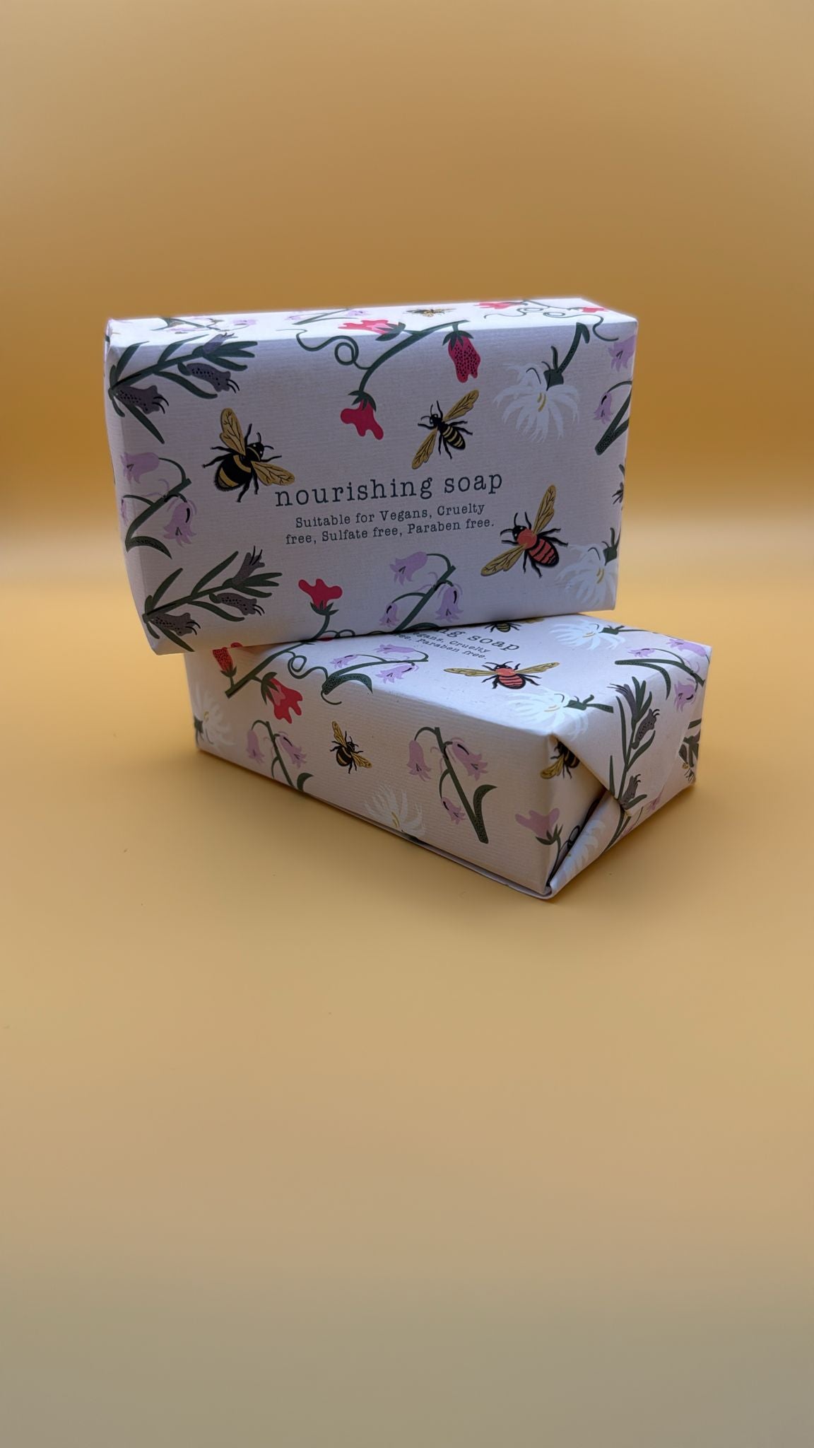 Two boxes of nourishing soap with floral and bee design on a yellow background