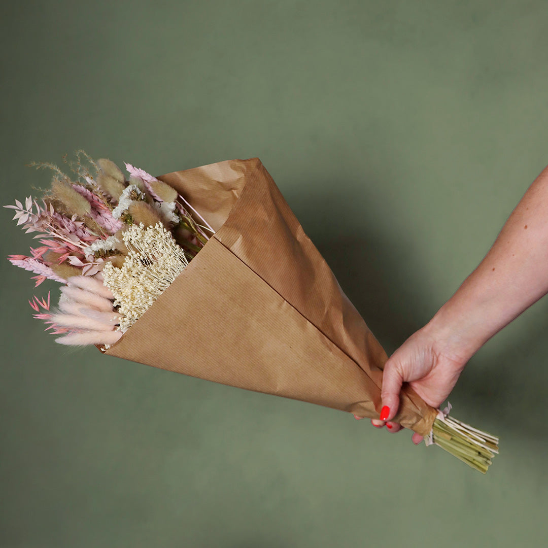 Bouquet of flowers wrapped in brown paper held by a hand against a green background
