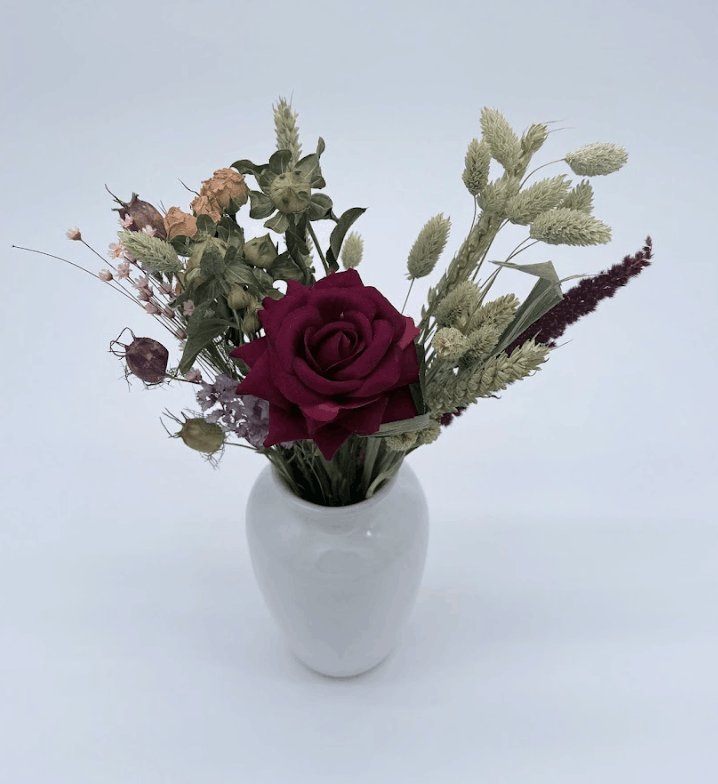 Bouquet of flowers with a red rose in a white vase on a light gray background