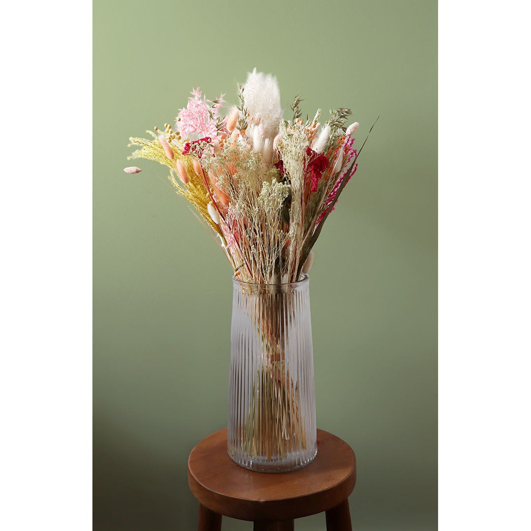 Bouquet of dried flowers in a clear vase on a wooden stool against a green background