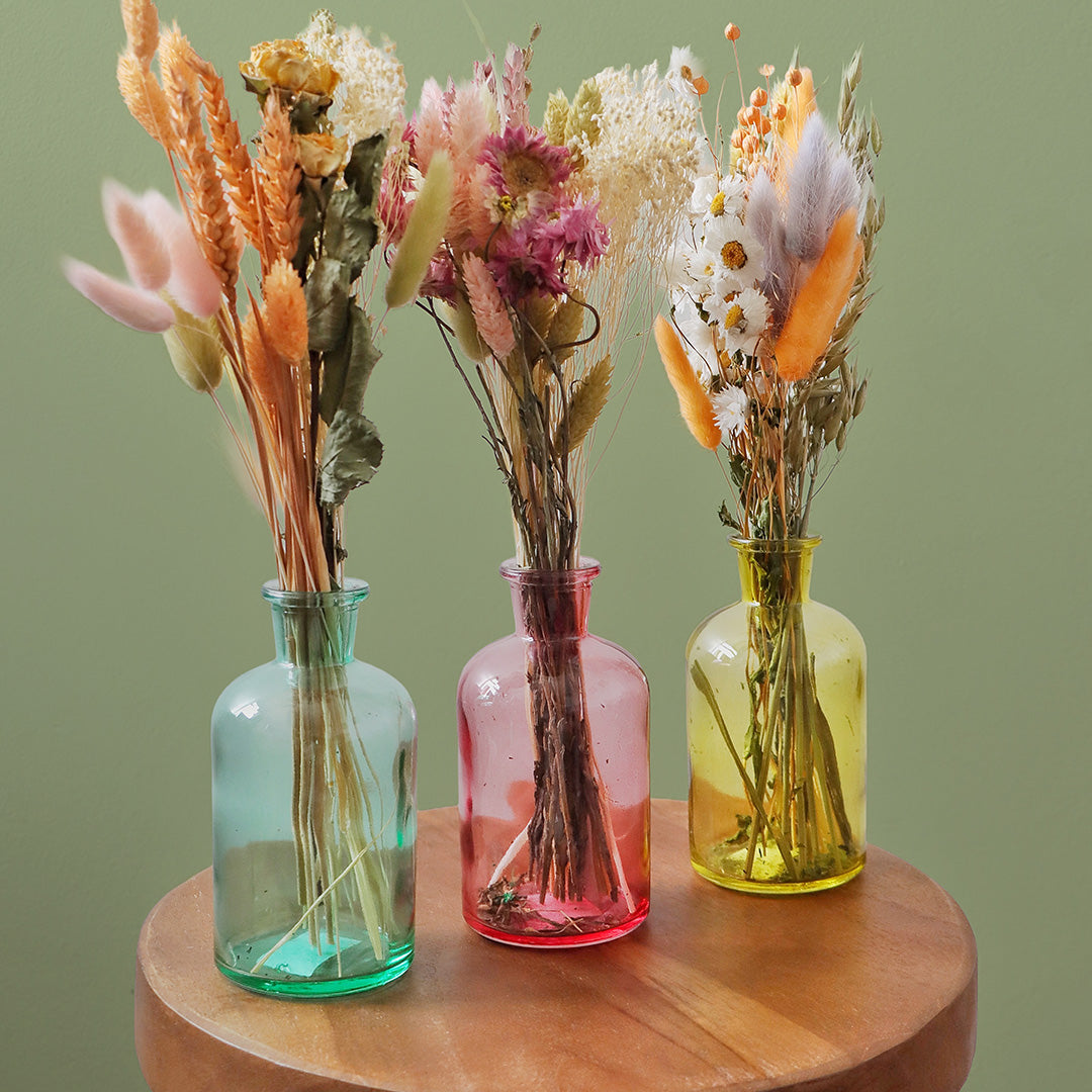 Three glass vases with dried flowers on a wooden surface against a green background