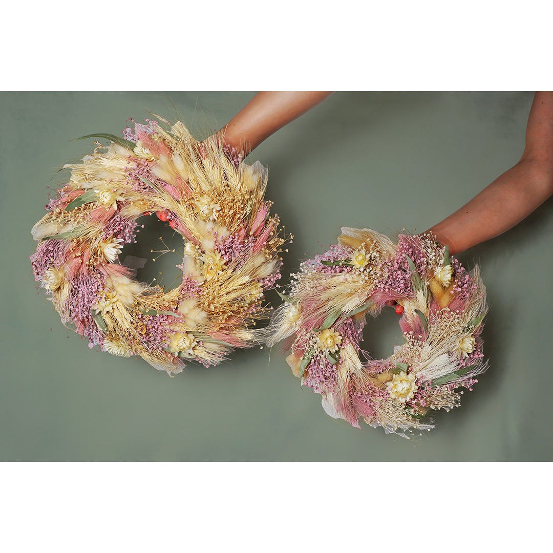 Two hands holding dried flower wreaths against a plain background