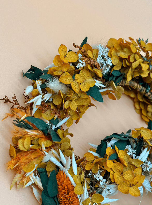 Decorative wreath with yellow flowers and green leaves on a beige background