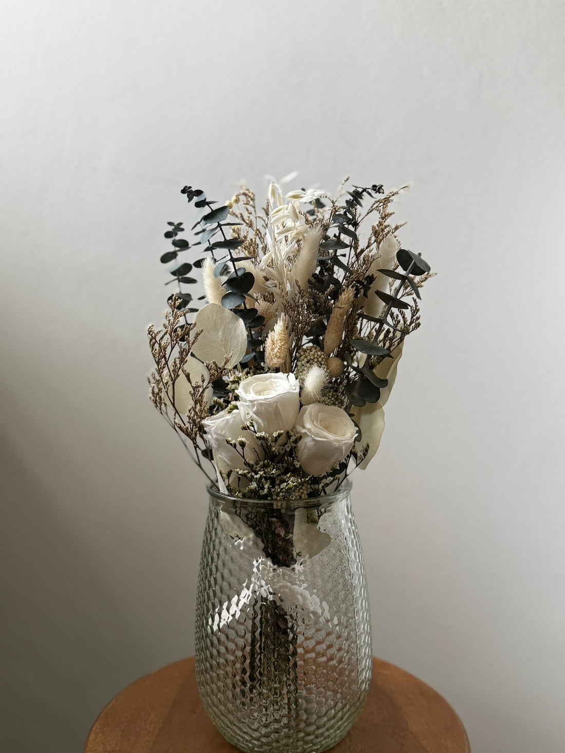 Decorative vase with dried flowers on a wooden surface against a plain background