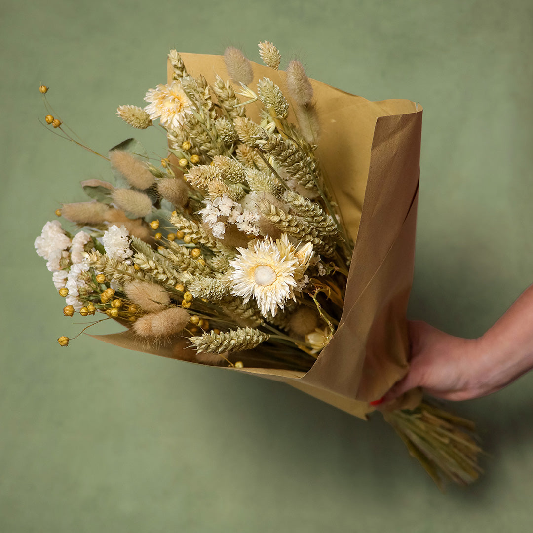 Bouquet of dried flowers wrapped in brown paper against a green background