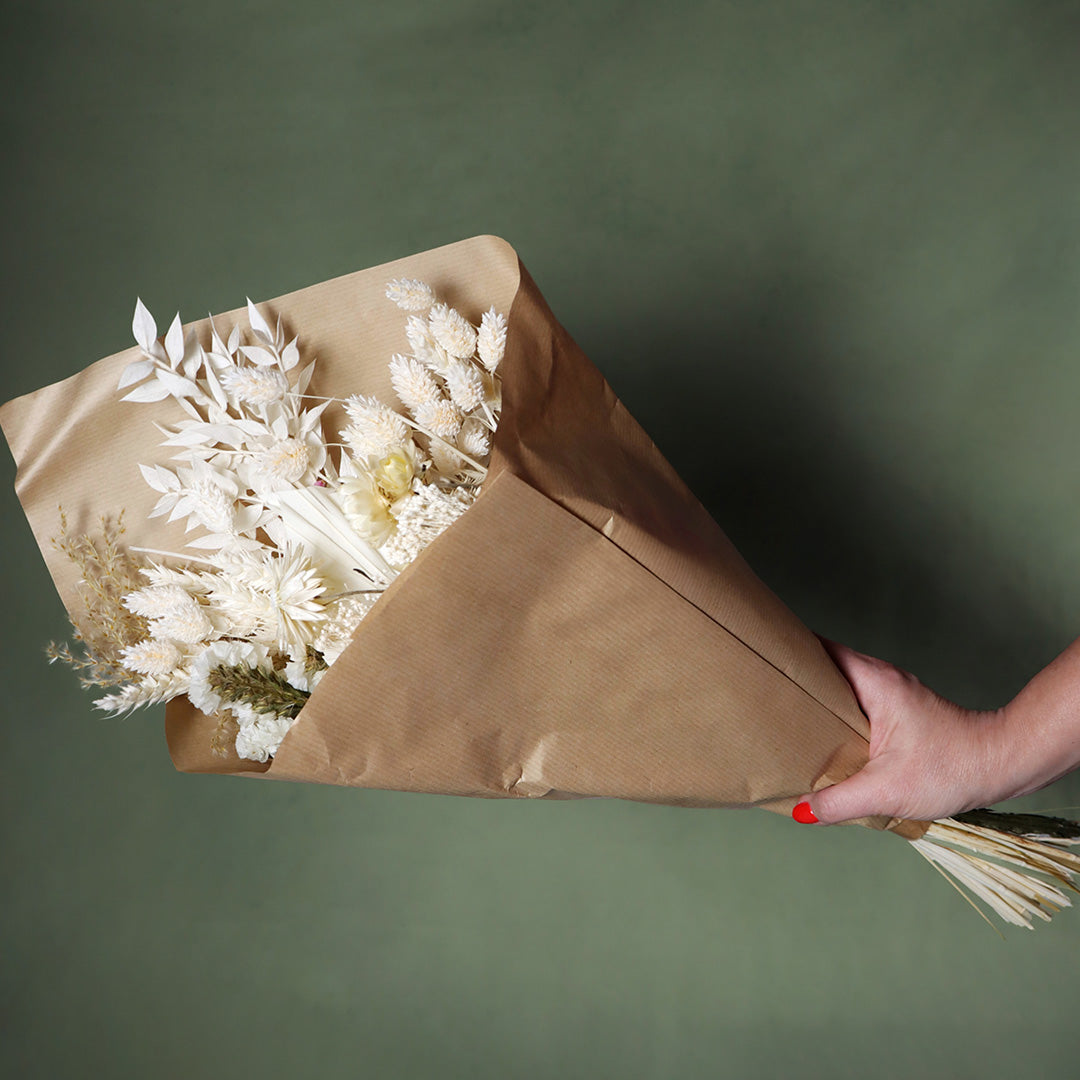 Bouquet of dried flowers wrapped in brown paper on a green background