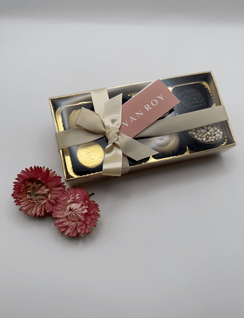 Belgian chocolate assortment gift box with gold ribbon bow and pink dried flowers on a light background